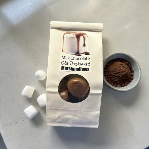 package of chocolate covered marshmallows on a counter with white marshamallows and ground cocoa powder